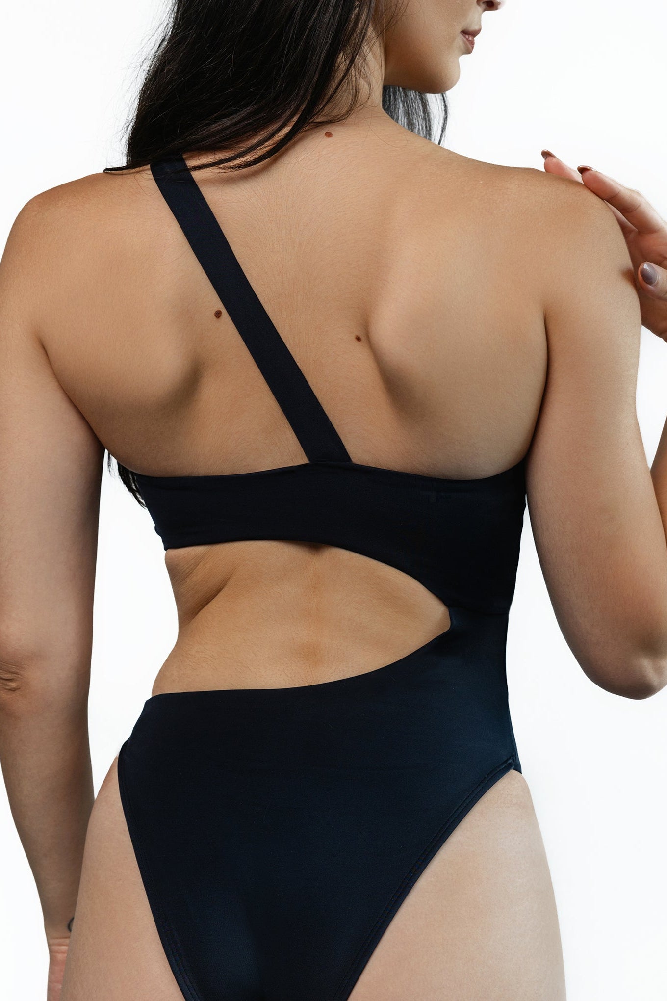 Closeup of the backside the Brooklyn cutout one-piece swimsuit in Black color. Model is standing in front of white background.